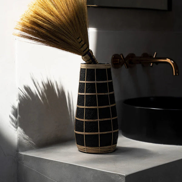 Vase with a broom on a concrete surface next to a black sink and faucet.