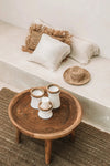 Wooden coffee table with decorative items on a beige sofa with pillows and a woven rug.