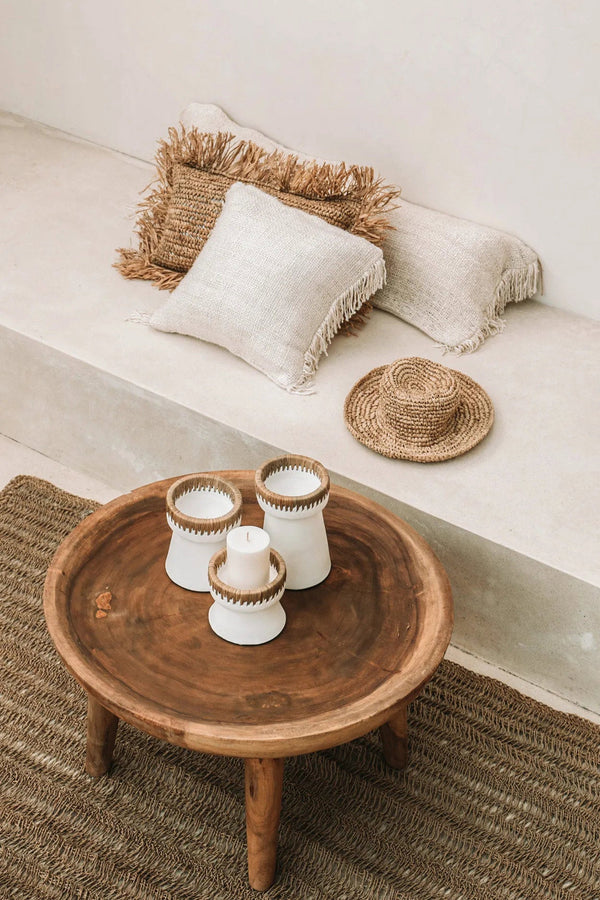 Wooden coffee table with decorative items on a beige sofa with pillows and a woven rug.