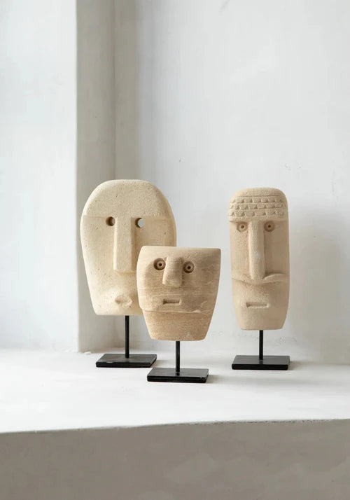Three stone face sculptures on stands against a white background