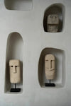 Three stone face sculptures in recessed shelves on a light gray wall.