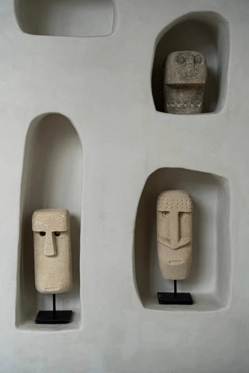 Three stone face sculptures in recessed shelves on a light gray wall.