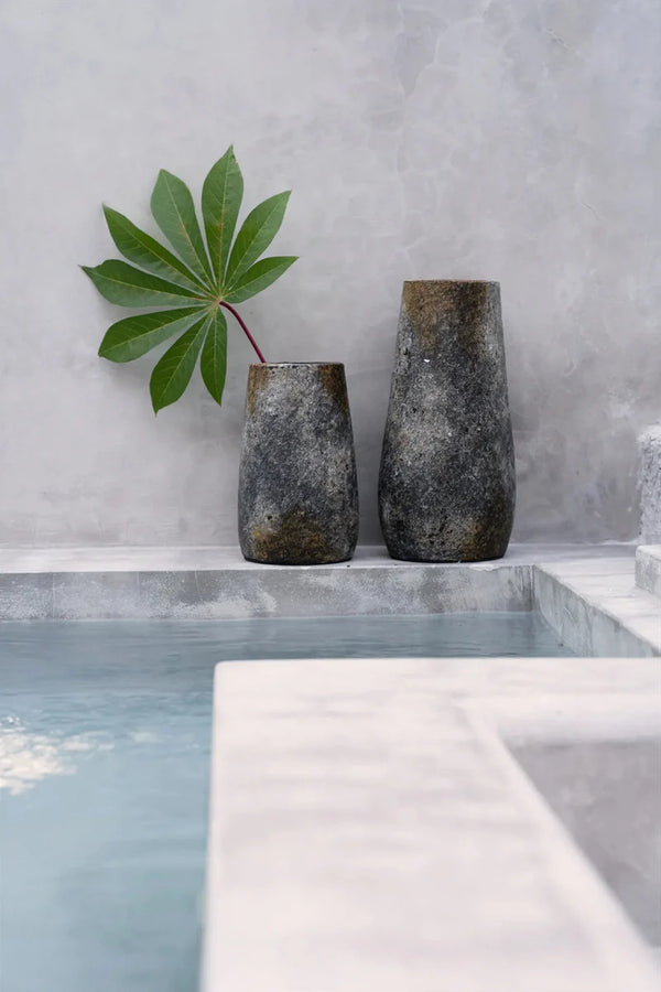 Two rustic vases with a leaf on a concrete ledge against a gray wall.