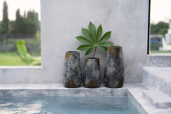 Three dark ceramic vases with a single green leaf on a windowsill.