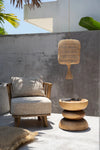Outdoor setting with a chair, small table, and hanging wicker lamp against a concrete wall.