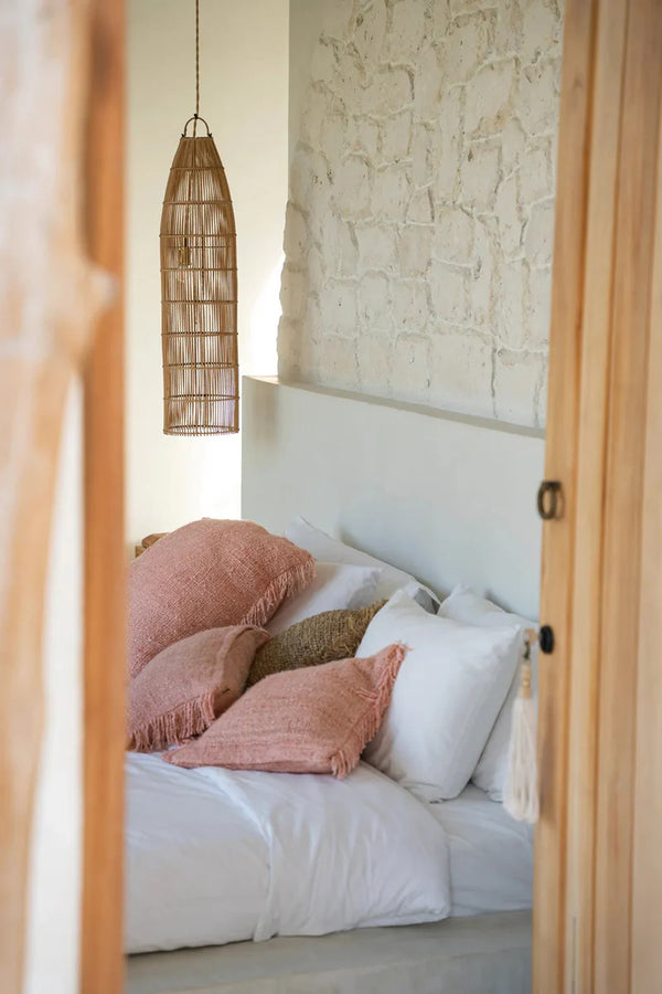 Bed with pink and white pillows against a stone wall