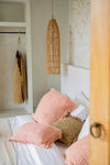 Bedroom with pink pillows and a hanging rattan lamp.