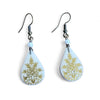Teardrop-shaped earrings with floral design on a light blue background