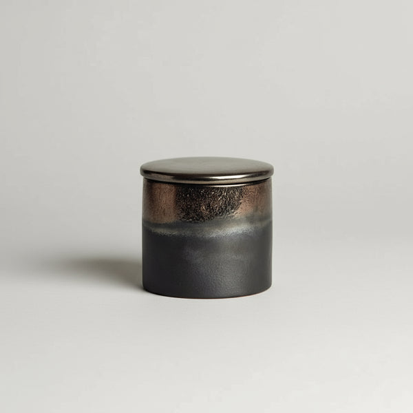 Black ceramic jar with lid on a stone surface
