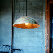 Vintage-style pendant light with a textured copper finish hanging against a brick wall.