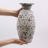 Person holding a decorative ceramic vase with intricate patterns on a light gray background