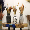 Three decorative vases with dried plants on a wooden table against a white wall.