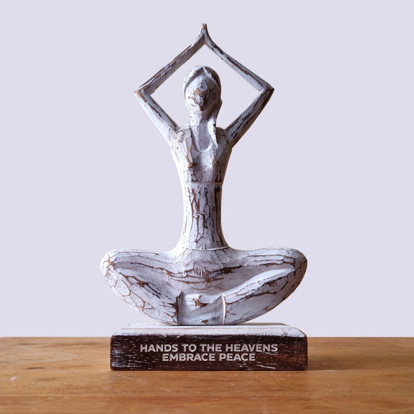 Decorative statue of a person in a meditative pose with 'Hands to the Heavens Embrace Peace' text on a wooden base.