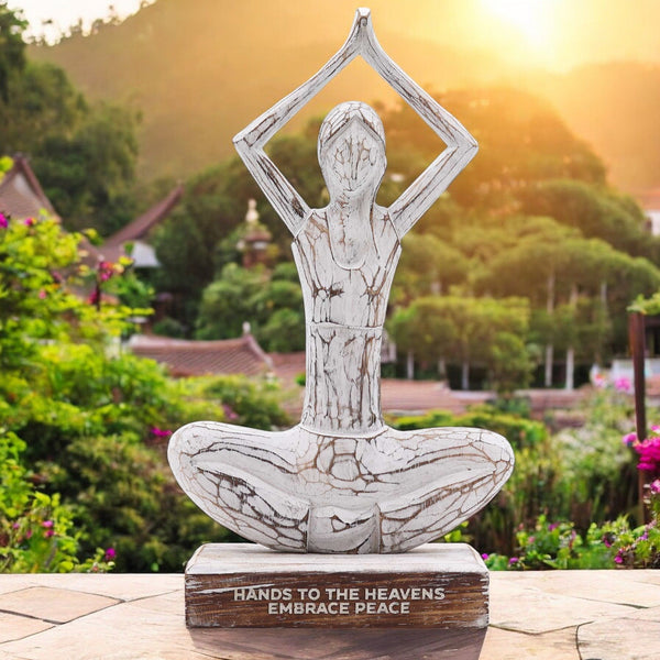 Statue of a person in a meditative pose with 'Hands to the Heavens Embrace Peace' text, set against a garden backdrop.