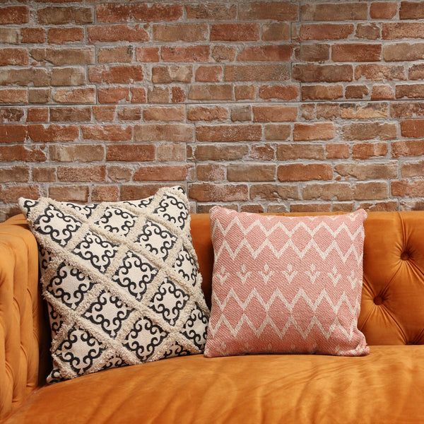 Two patterned pillows on an orange couch against a brick wall.