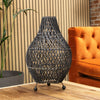 Woven rattan table lamp on a wooden surface with an orange sofa and plant in the background
