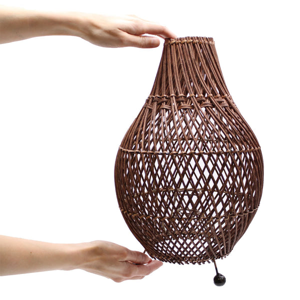 Woven brown lampshade held by a hand on a white background