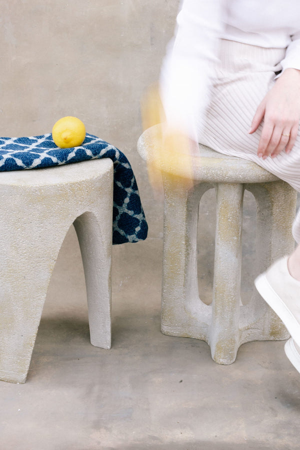Person sitting on a textured stool with a lemon and towel, next to another stool.