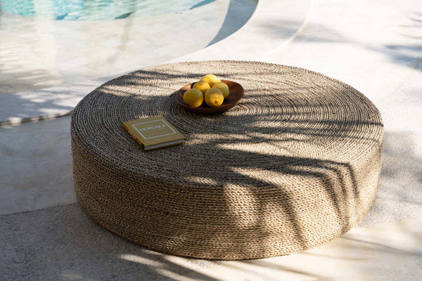 Round woven ottoman with a small bowl of lemons on a light surface