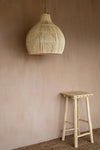 Woven pendant light hanging above a wooden stool against a beige wall.