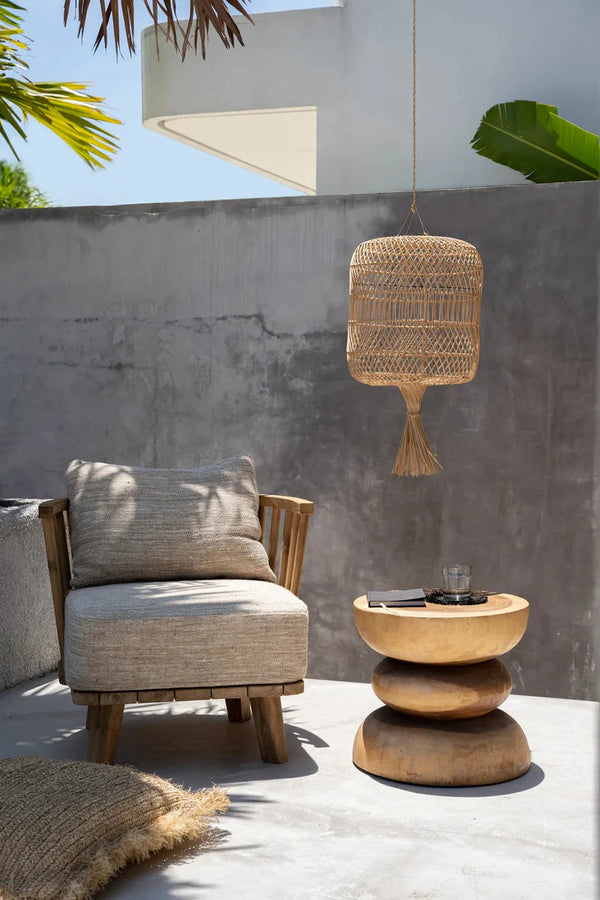 Outdoor setting with a chair, small table, and hanging wicker lamp against a concrete wall.