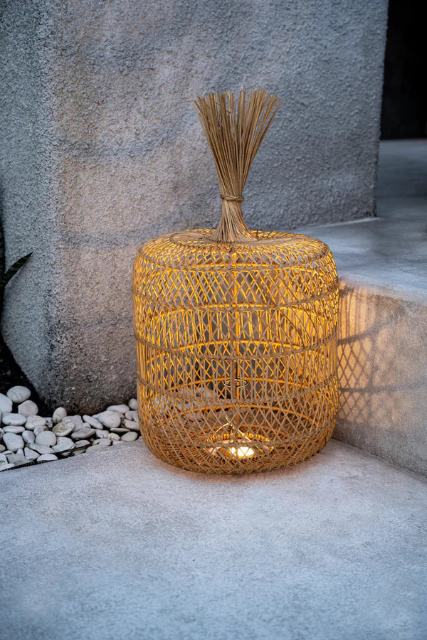Woven outdoor stool with a bundle of twigs on top against a stone wall.