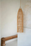 Woven bamboo pendant light hanging against a white wall with a wooden bench below.