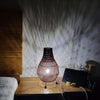 Woven table lamp on a wooden surface with a blurred background
