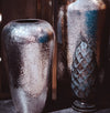 Two metallic vases with textured surfaces on a reflective surface.