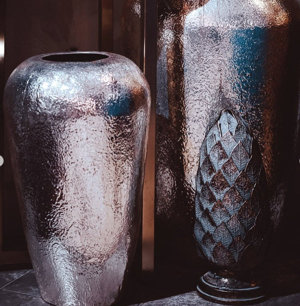 Two metallic vases with textured surfaces on a reflective surface.