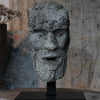 Stone sculpture of a face on a stand with a textured wall background