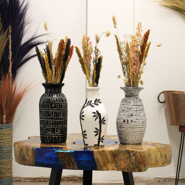 Three decorative vases with dried plants on a wooden table against a white wall.