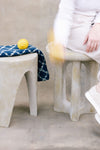 Person sitting on a textured stool with a lemon and towel, next to another stool.